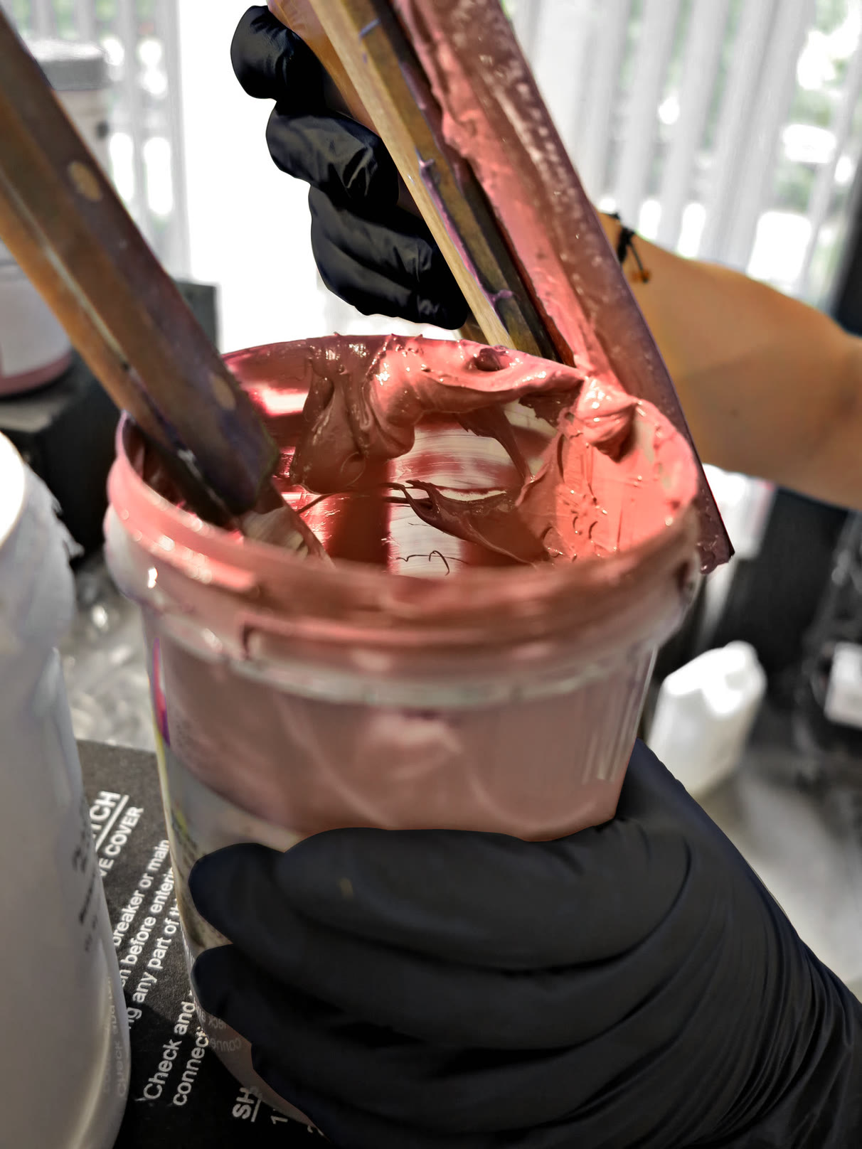 Pot d'encre de sérigraphie rose ouvert, spatule à la main, à l'atelier du 12e