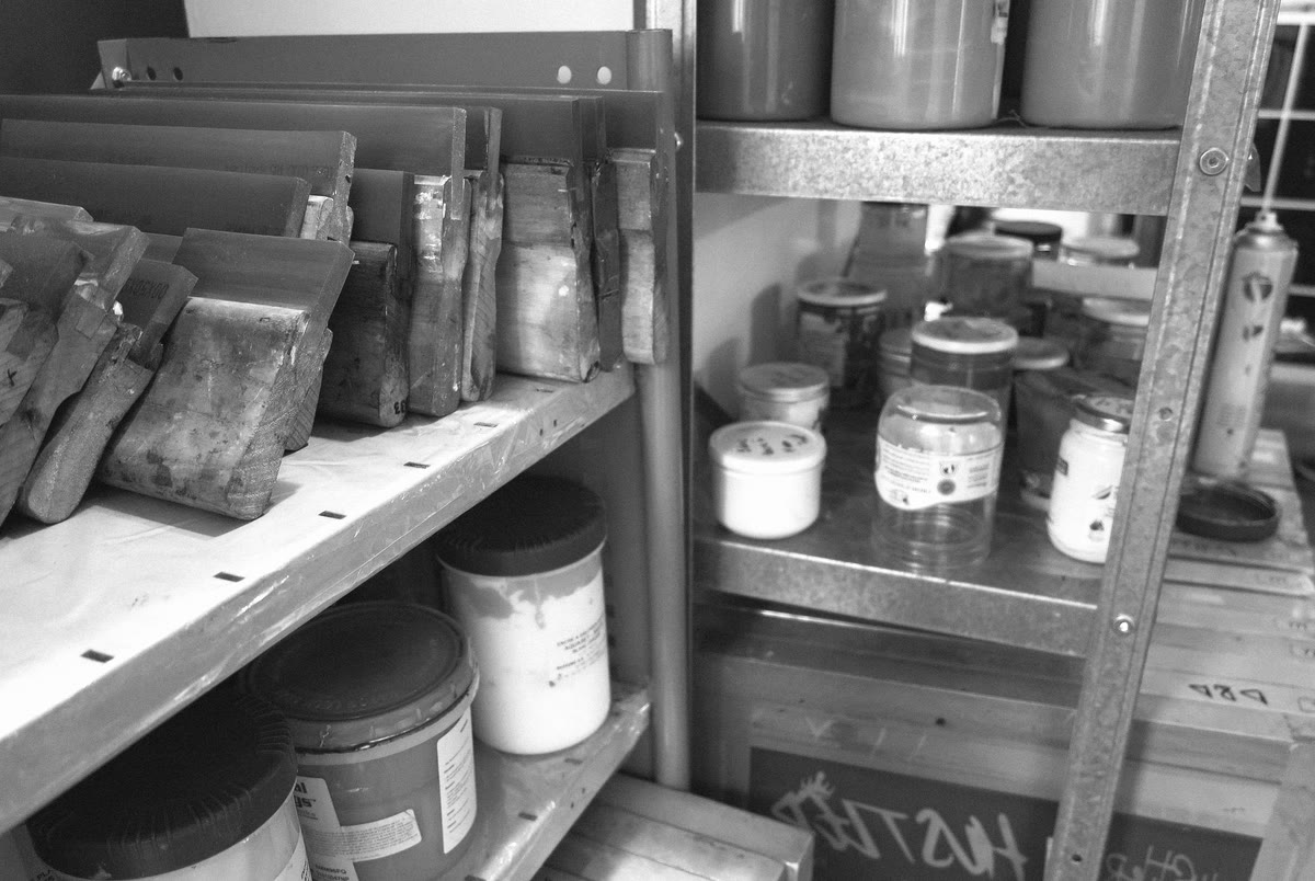Étagères d'écrans de sérigraphie et pots d'encre rangés à l'atelier