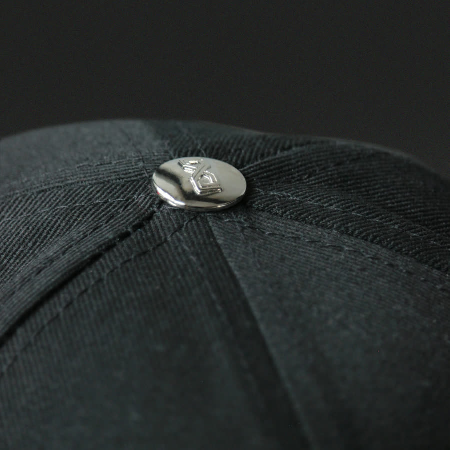 Bouton métallique gravé au sommet d'une casquette brodée