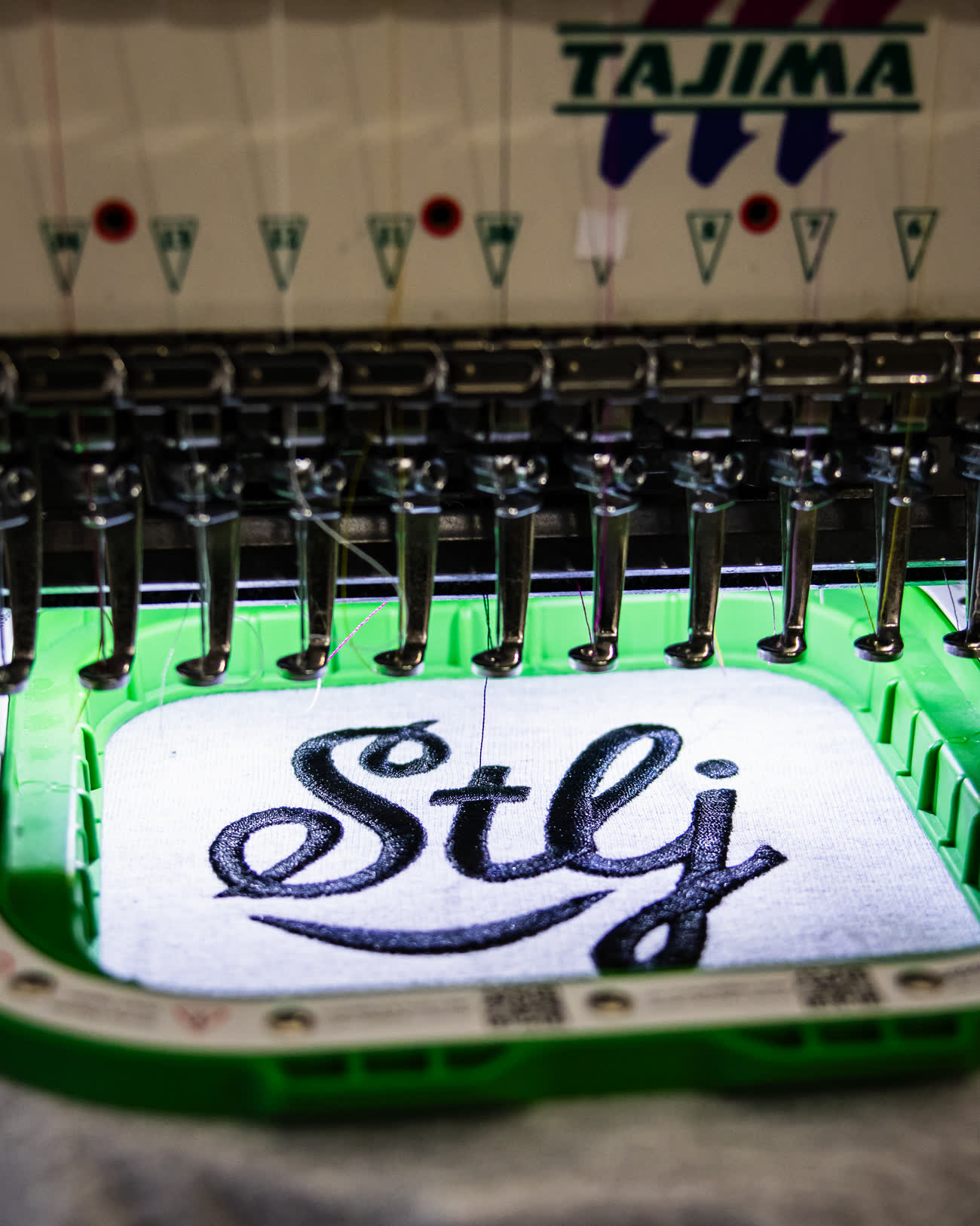 Brodeuse industrielle Tajima en train de broder un logo manuscrit sur un textile blanc tendu dans son cadre