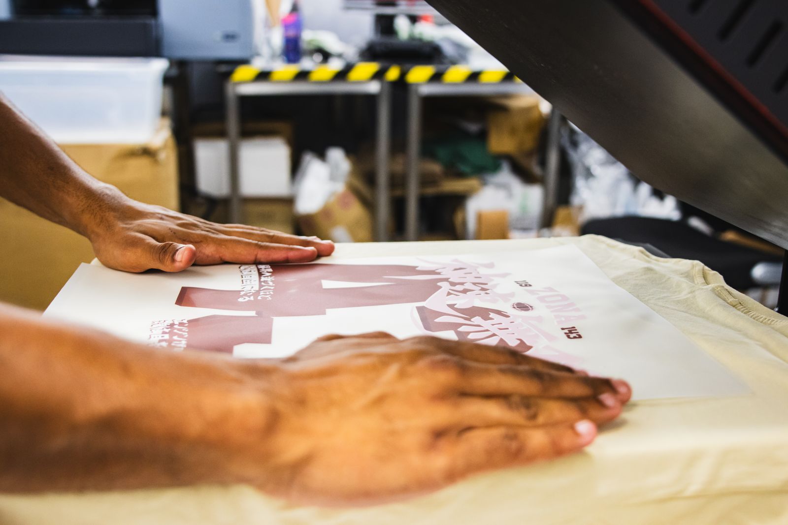 Deux mains lissent le film posé sur le t-shirt, sur le plateau de la presse