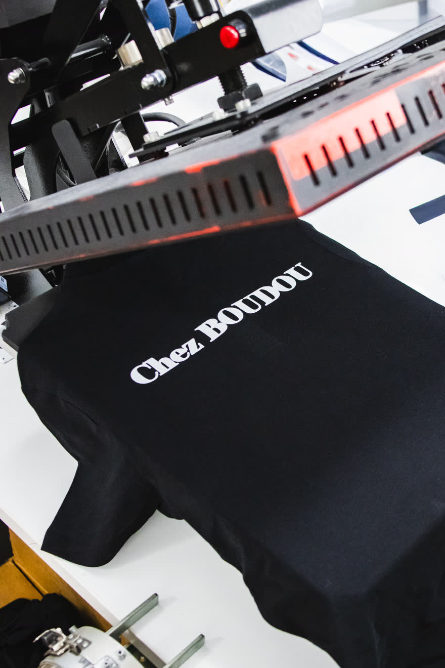 Presse à chaud appliquant le marquage Chez Boudou sur le polo noir