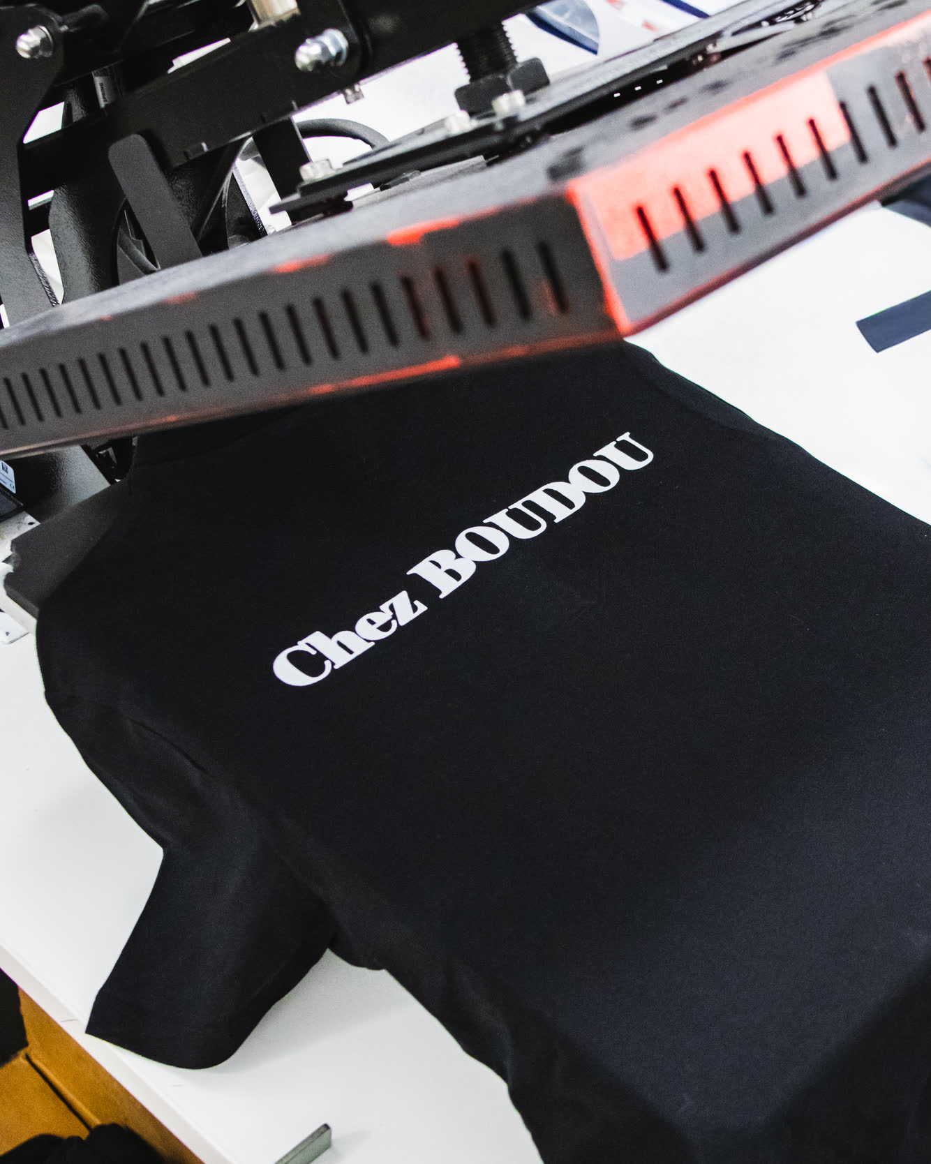 Presse à chaud abaissée sur un polo noir portant le marquage « Chez Boudou » en blanc