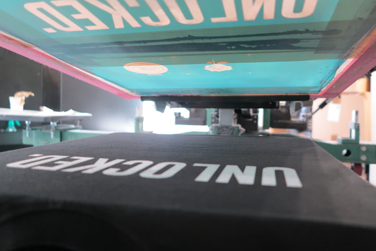 Écran de sérigraphie relevé au-dessus du t-shirt, laissant voir le marquage blanc qui vient d'être tiré